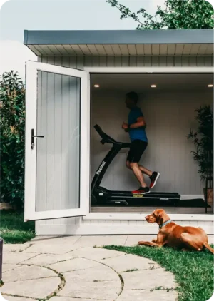 Man running on treadmill in garden room with dog at home with him